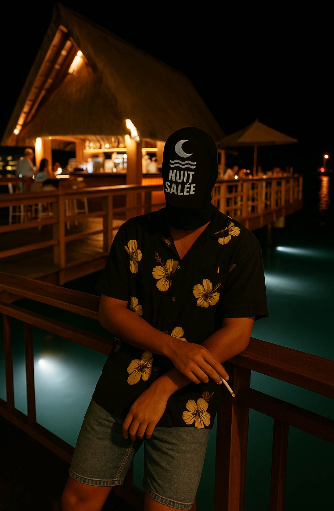 Nuit Salée at night beside a lagoon-side bar, lit by warm lamps and underwater lights.